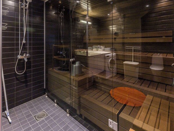 A modern bathroom with a glass shower enclosure, a built-in washing machine, and a wooden vanity.