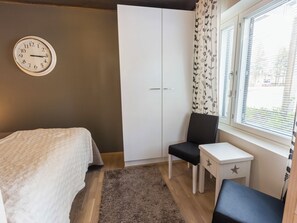 A bedroom with a bed, a chair, a small table, a wardrobe, and a window with curtains.