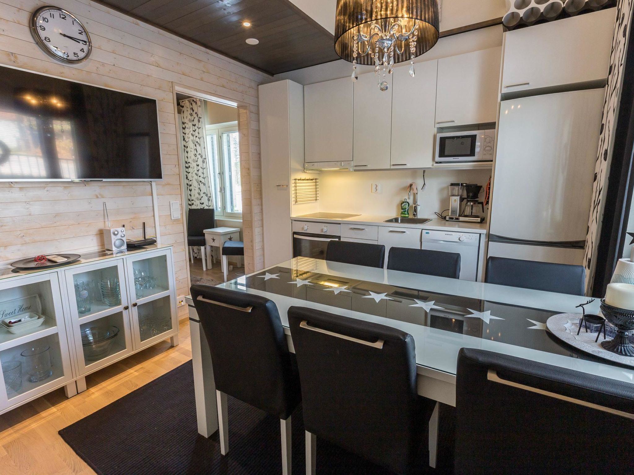 A modern kitchen with white cabinets, a central island with chairs, a chandelier, and a clock on the wall.