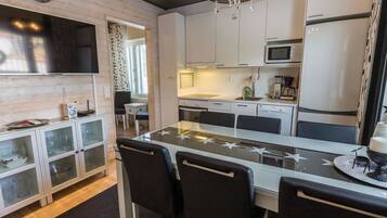 A modern kitchen with white cabinets, a central island with chairs, a chandelier, and a clock on the wall.