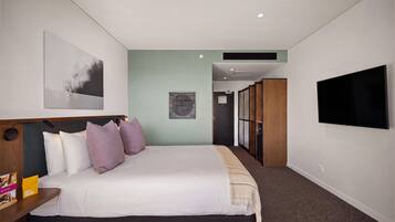 Habitación de hotel moderna con una cama grande, televisor de pantalla plana y vista al pasillo.