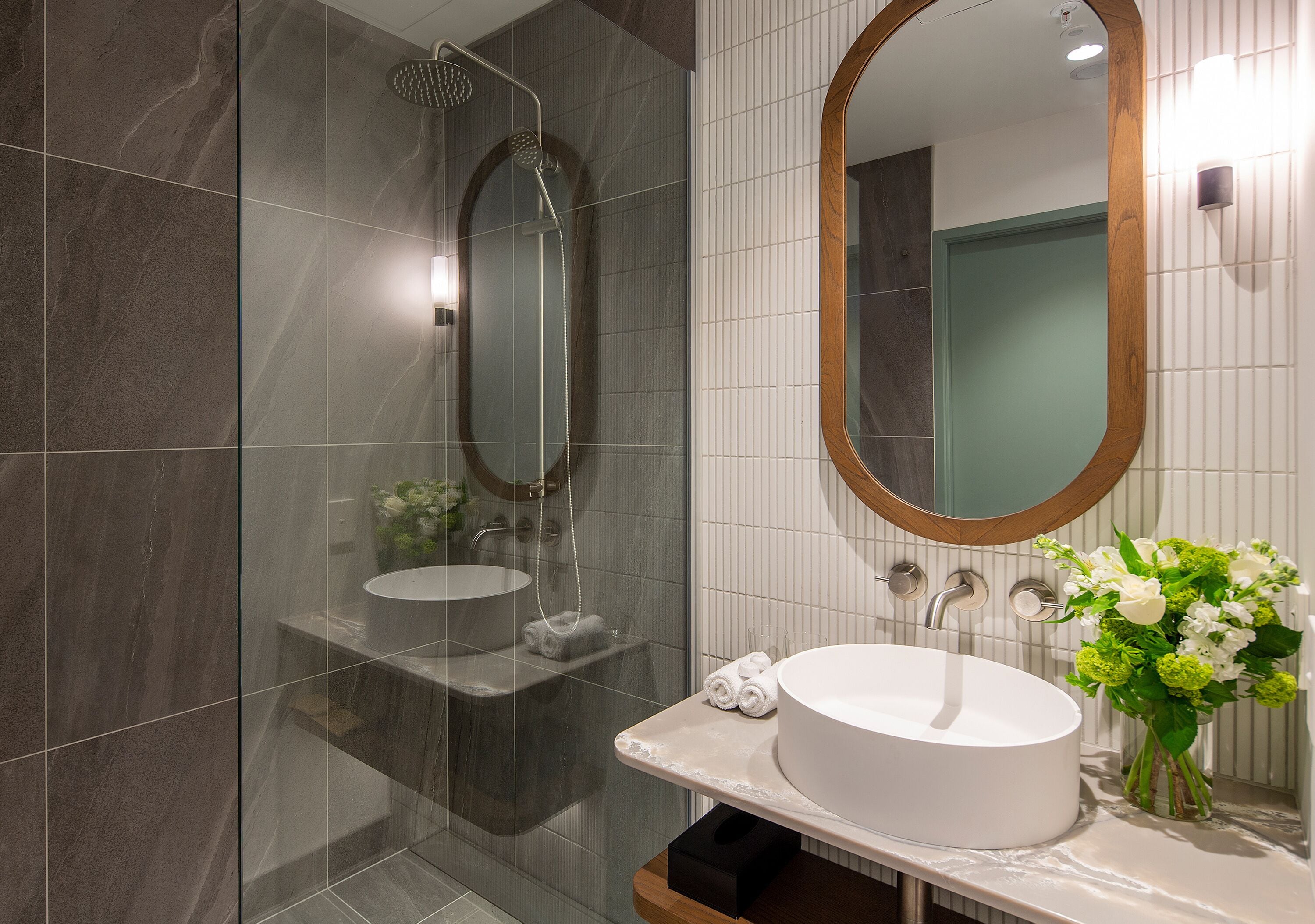A modern bathroom with a glass-enclosed shower, a white sink, and a mirror with a wooden frame.