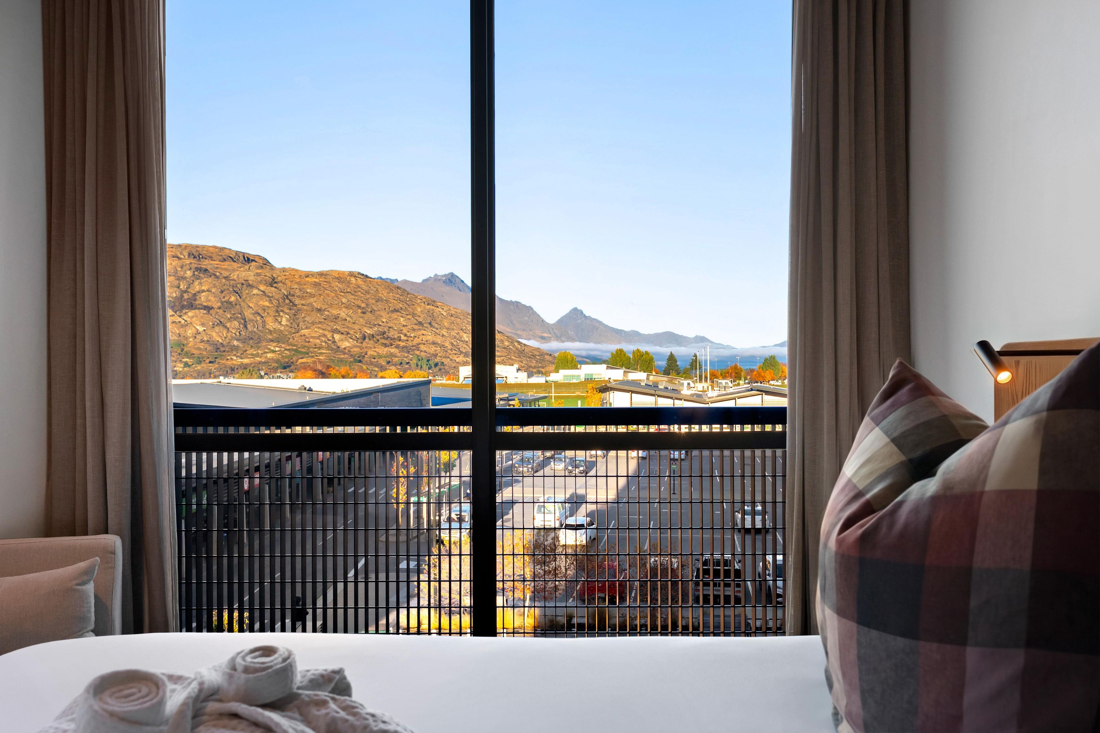 A hotel room with a large window offering a view of mountains and a parking area.