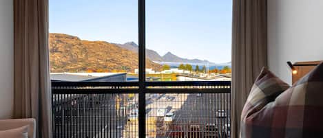 A hotel room with a large window offering a view of mountains and a parking area.