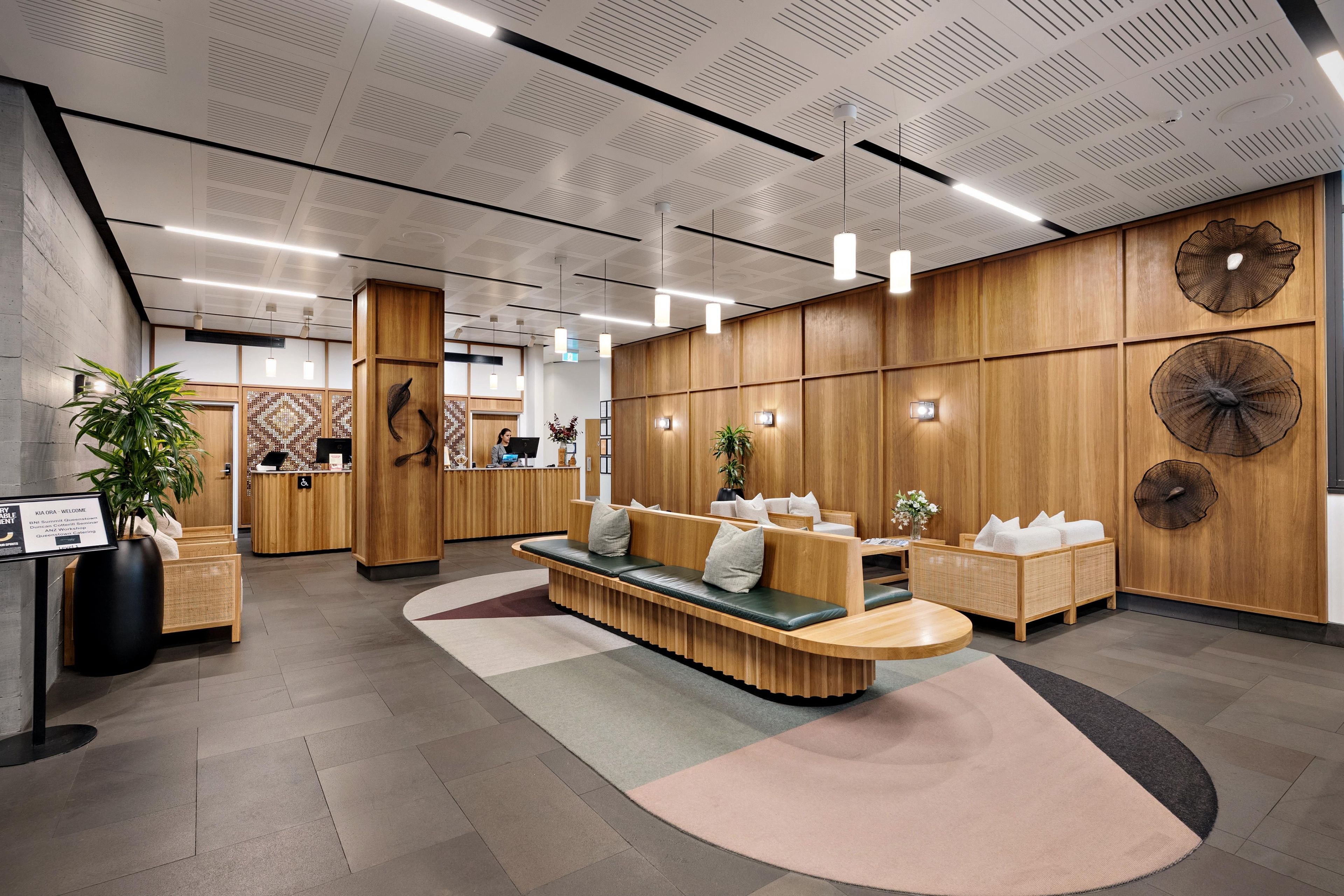 Un área de recepción moderna con mostrador de madera, zona de estar y paneles decorativos en la pared.