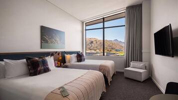Habitación de hotel con dos camas, un televisor de pantalla plana, un ventanal con vistas a la montaña y una mesita.