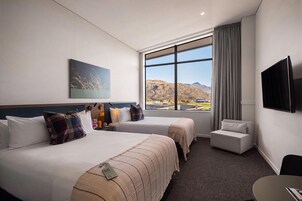 Habitación de hotel con dos camas, un televisor de pantalla plana, un ventanal con vistas a la montaña y una mesita.