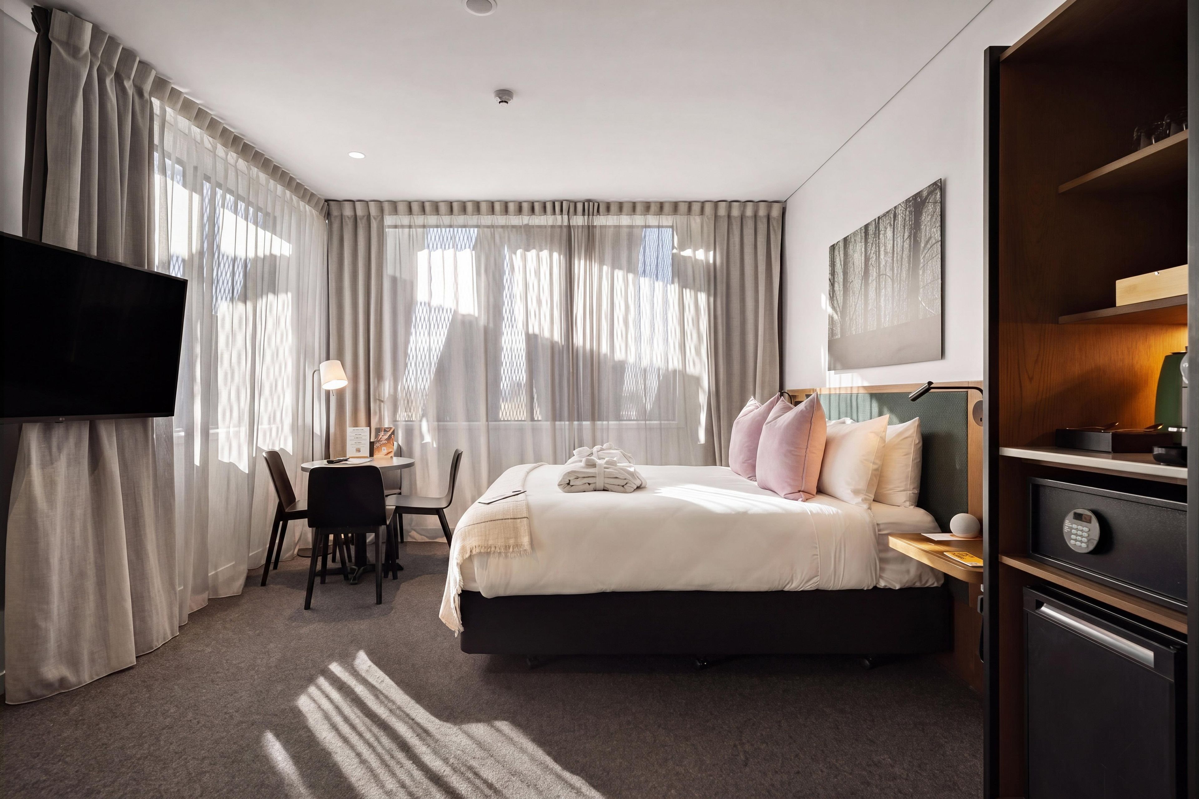 Ein Hotelzimmer mit Bett, Schreibtisch, Stuhl, Fernseher und einem Gemälde an der Wand.