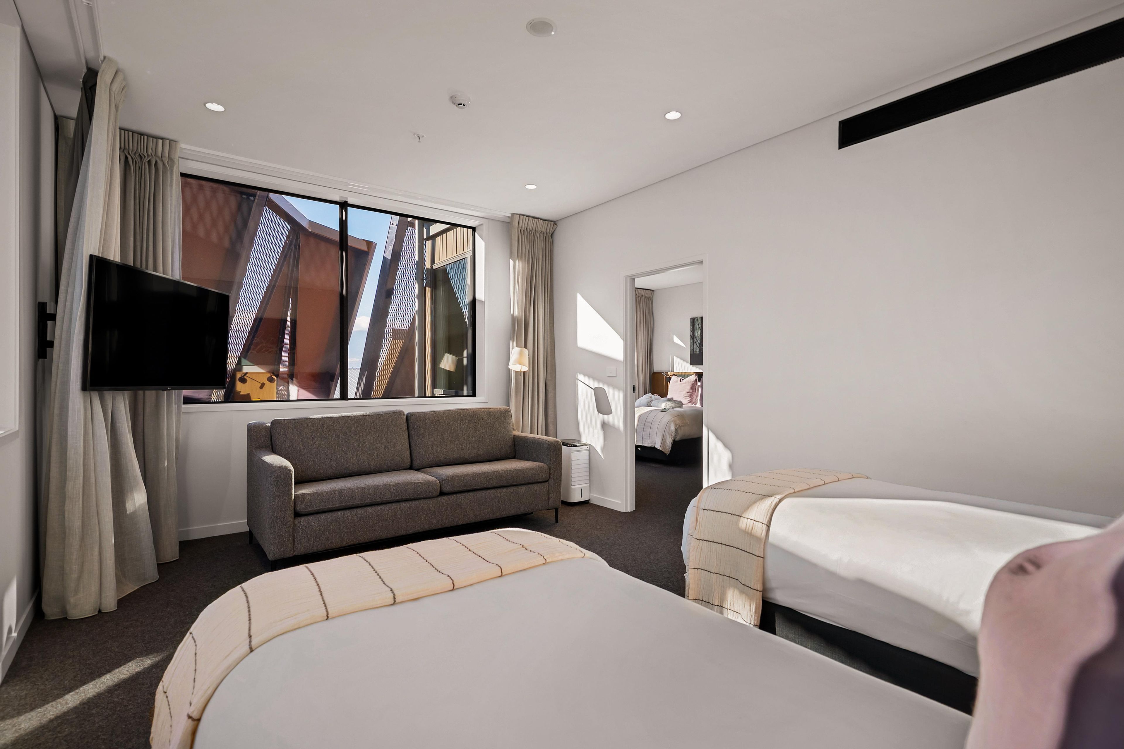 Une chambre d’hôtel avec un canapé, un lit, une télévision et une fenêtre avec des rideaux.