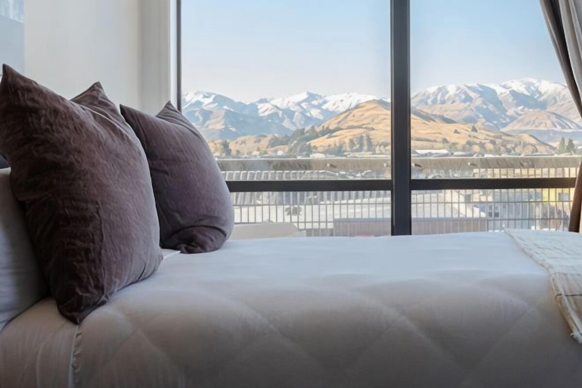 A bed with pillows and a view of snow-capped mountains through a window.