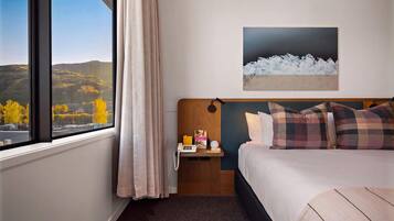 Habitación de hotel con cama, mesita de noche, un cuadro y vistas al exterior.