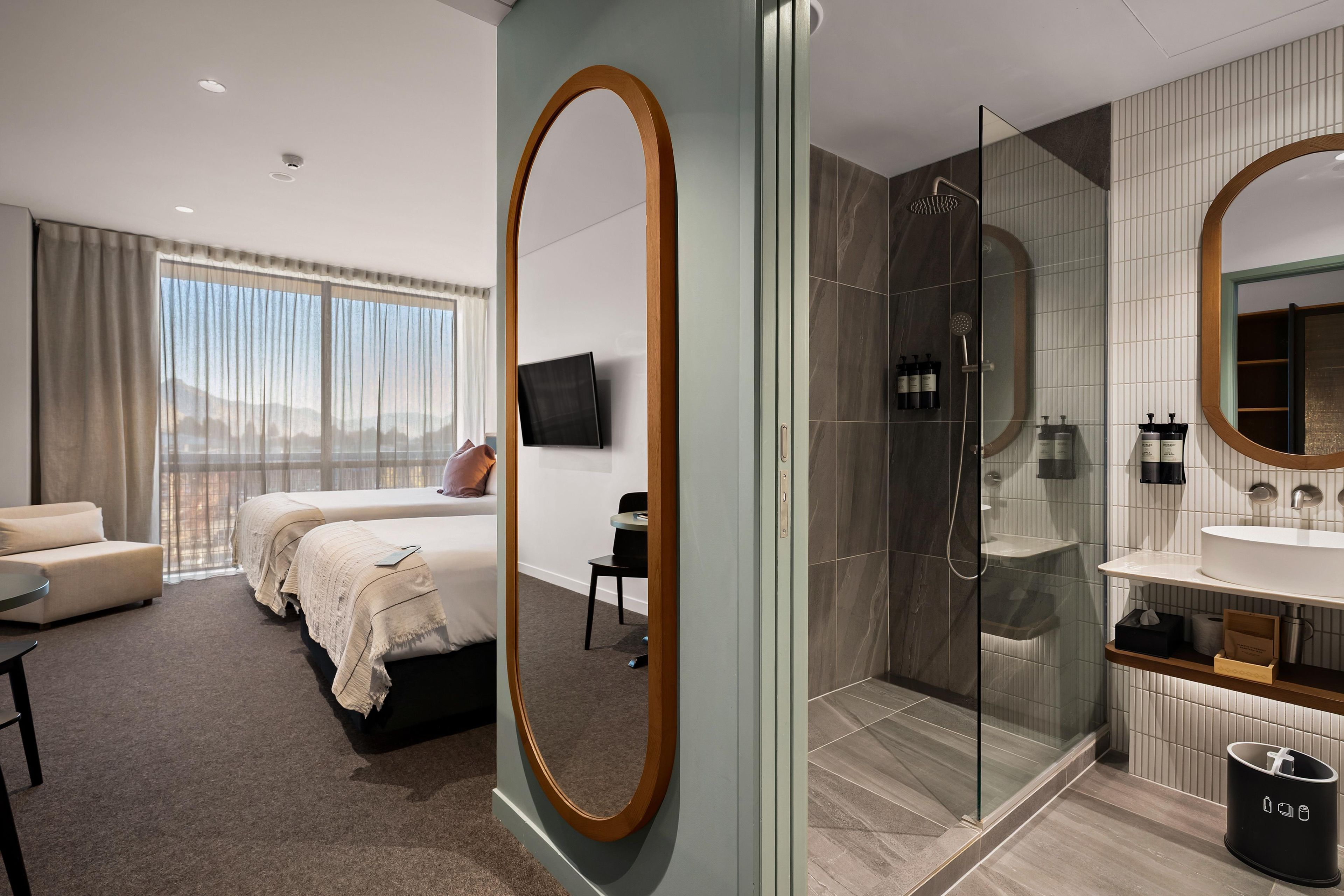 Een moderne hotelkamer met een groot bed, een apart zithoekje, een douche en een badkamer met een grote spiegel.