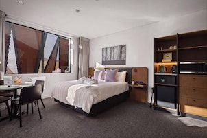 Ein Hotelzimmer mit einem Bett, einem Schreibtisch, einem Stuhl, einem Bücherregal und einem Gemälde an der Wand.