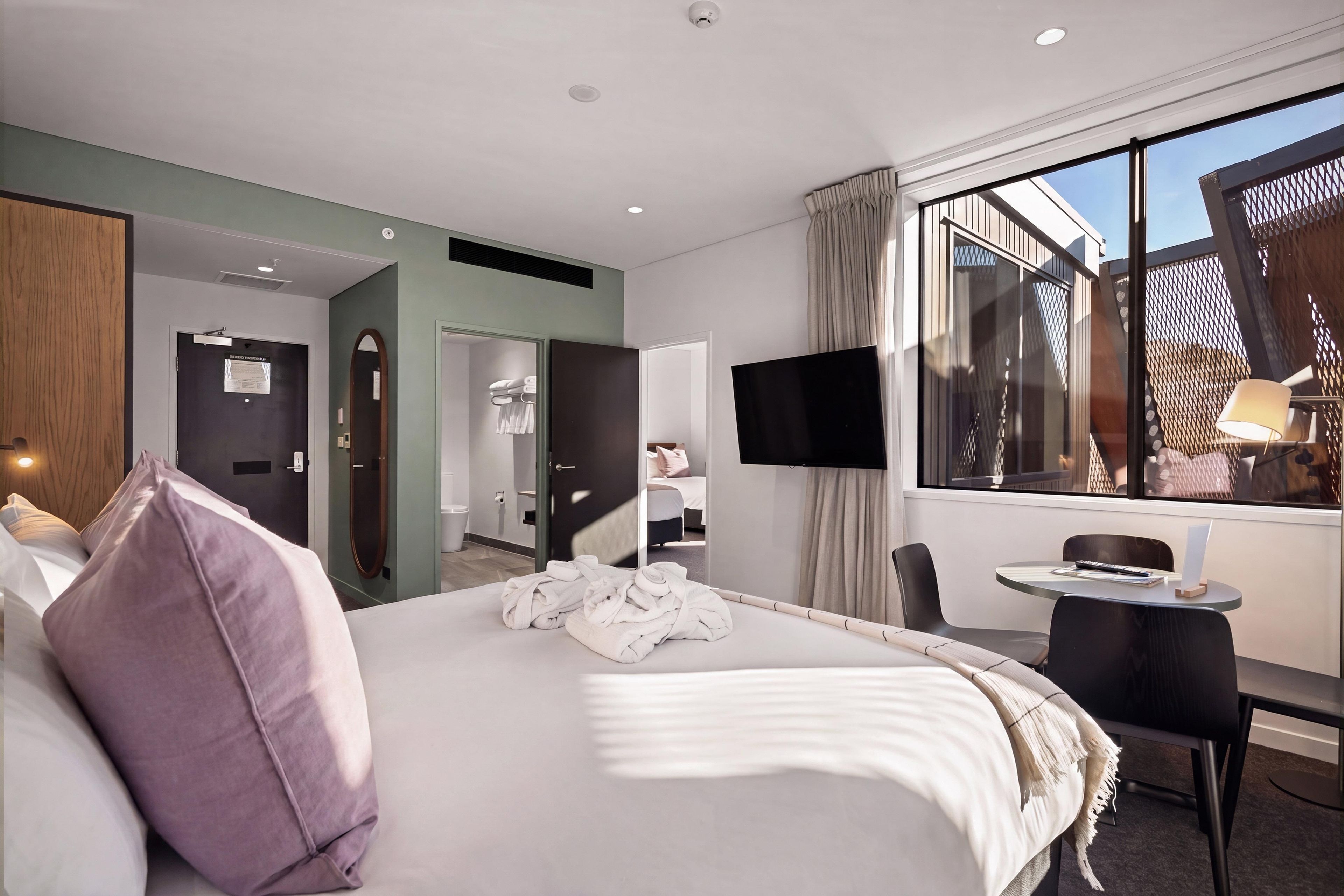 Habitación de hotel con cama, escritorio, silla, televisión y ventana con vista al exterior.