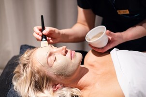 A person lying down with a facial mask being applied.