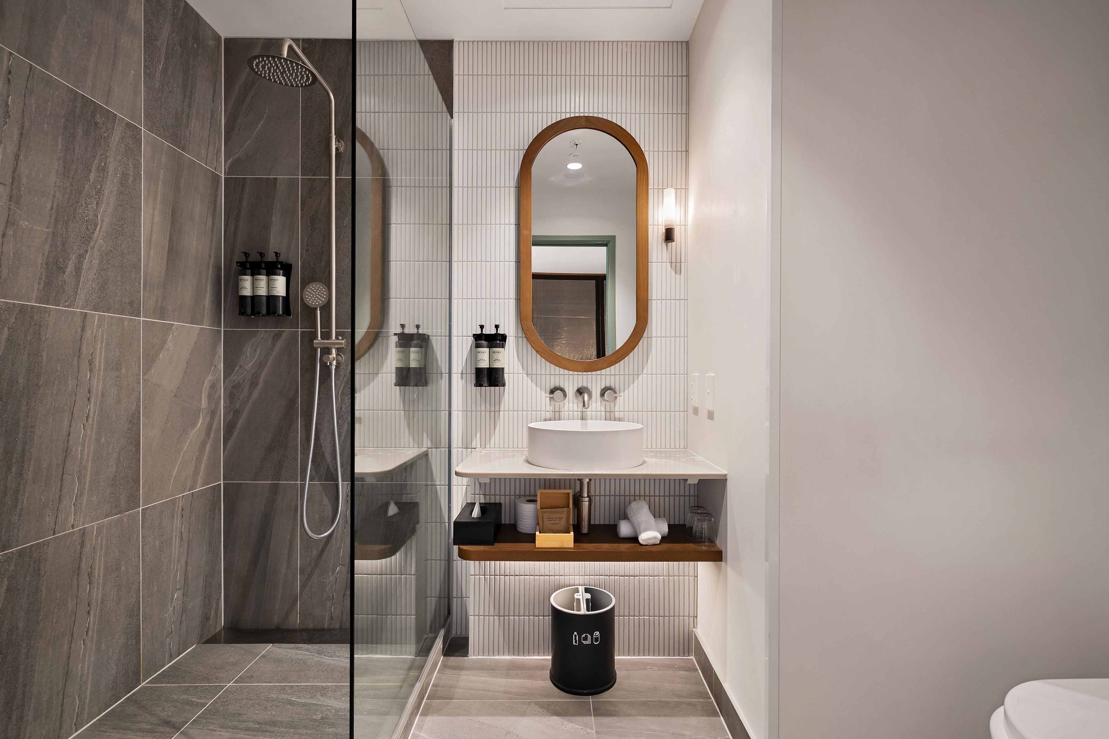 Un baño moderno con ducha de vidrio, un lavabo blanco y un espejo con marco de madera.