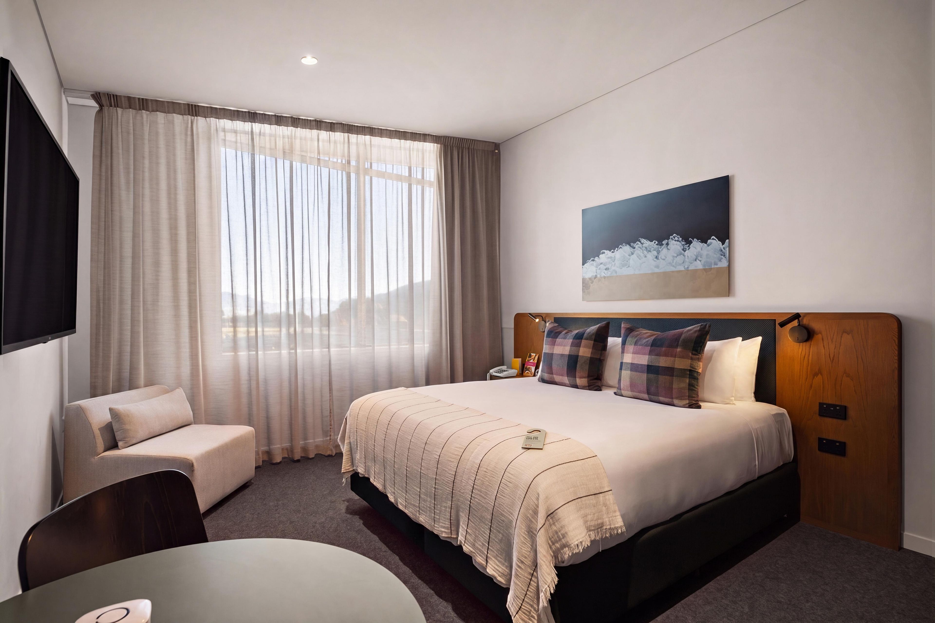 Habitación de hotel con cama, escritorio, silla, televisor y ventana con cortinas.