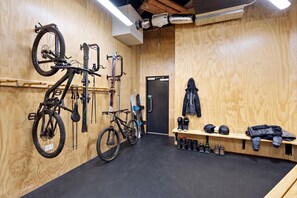 A room with wooden walls, a black carpet, a bench with helmets, and bicycles mounted on the wall. - Sudima Queenstown Five Mile (Queenstown)