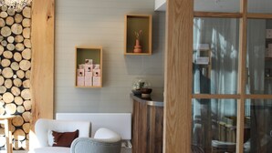 A cozy room with a white sofa, a grey chair, wooden wall panels, and a glass cabinet with items on top. - Sudima Queenstown Five Mile (Queenstown)