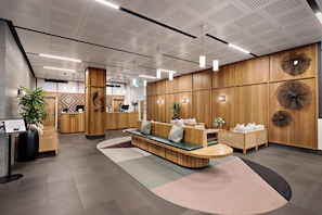 A modern reception area with a wooden reception desk, seating area, and decorative wall panels. - Sudima Queenstown Five Mile (Queenstown)