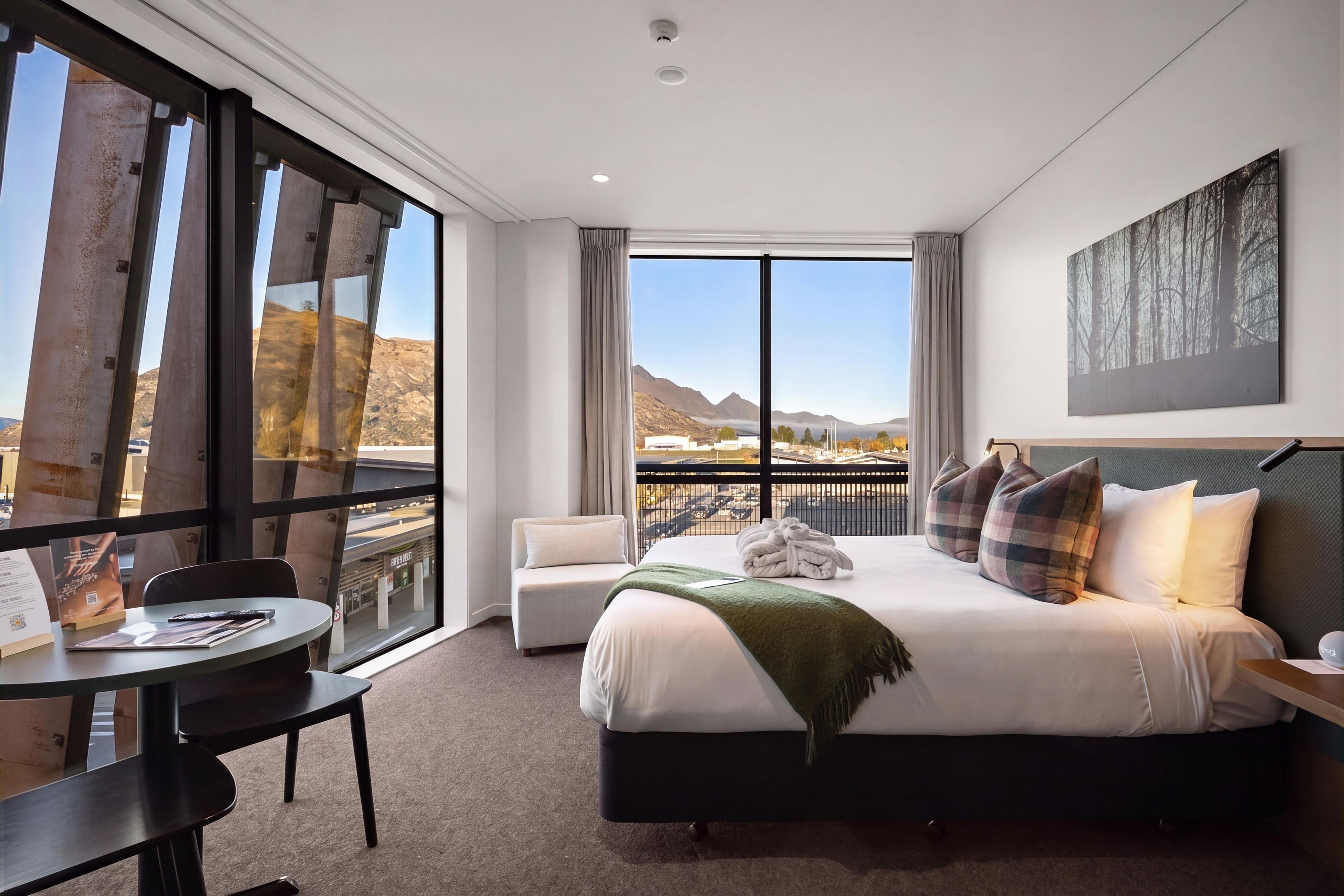 Habitación de hotel con una cama grande, un escritorio y vistas a las montañas a través de la ventana.
