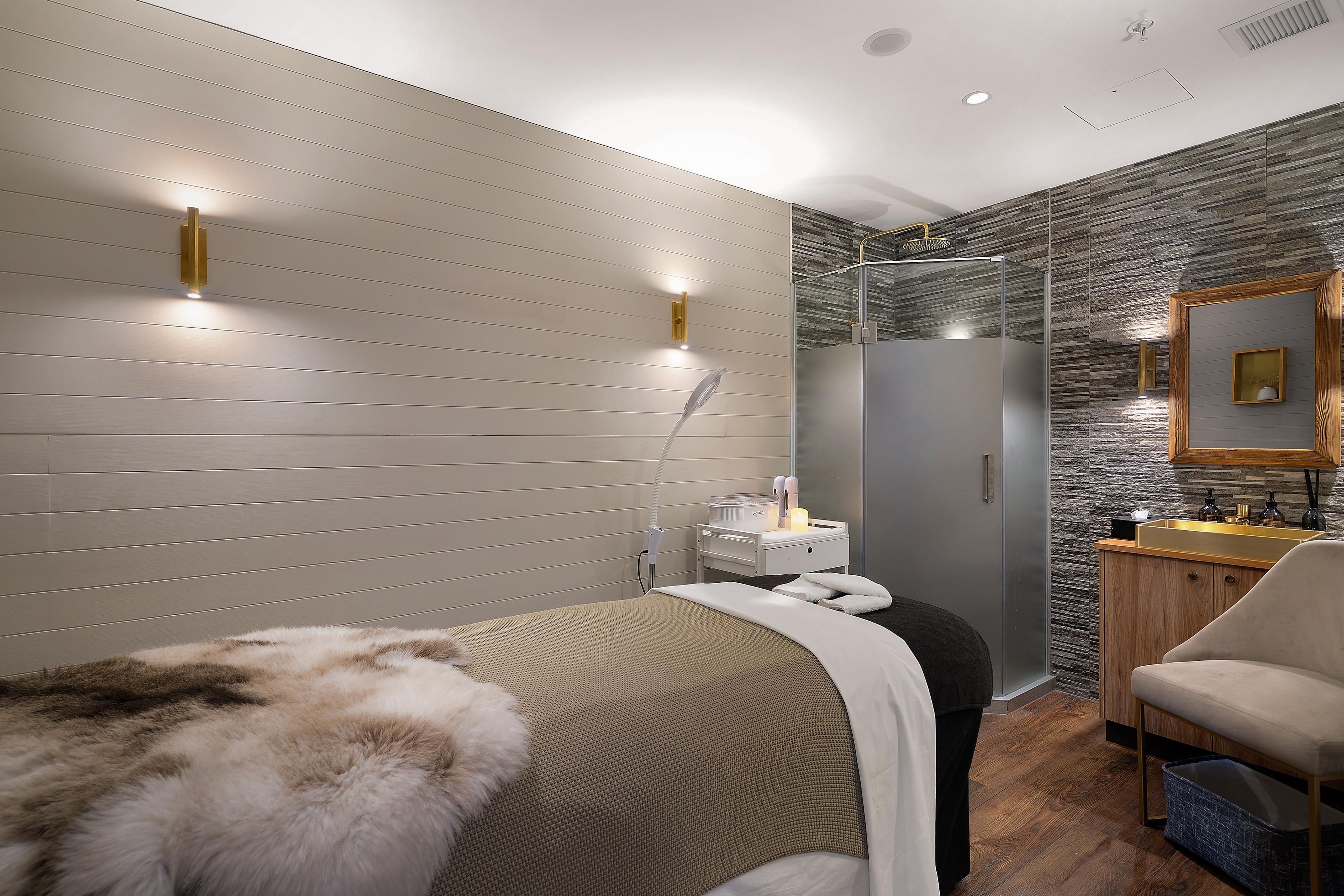 A modern bedroom with a bed, a vanity, and a shower.