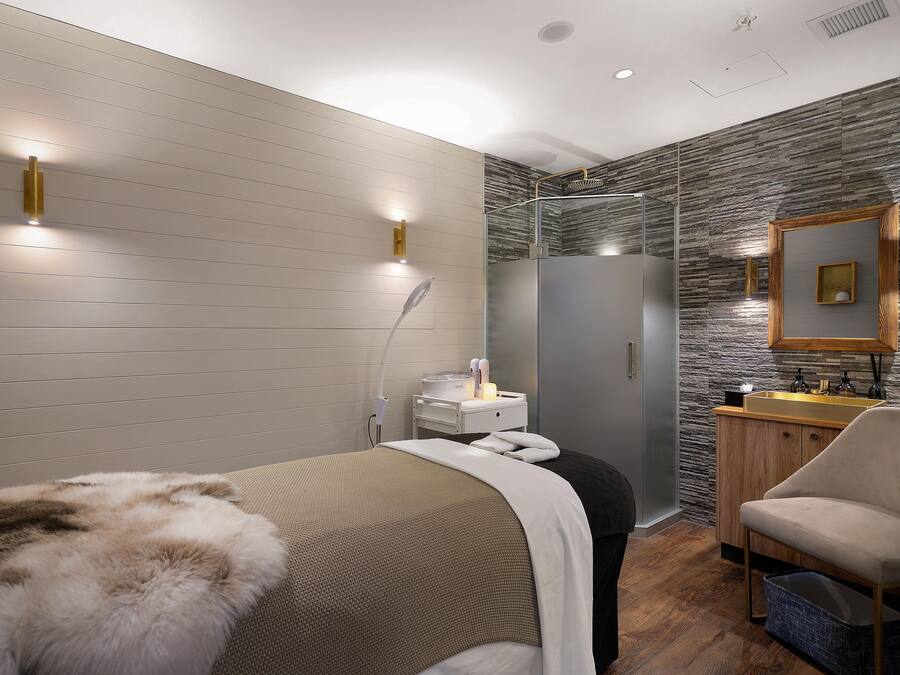 A modern bedroom with a bed, a vanity, and a shower.