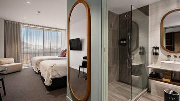 A modern hotel room with a large bed, a separate seating area, a shower area, and a bathroom with a large mirror.