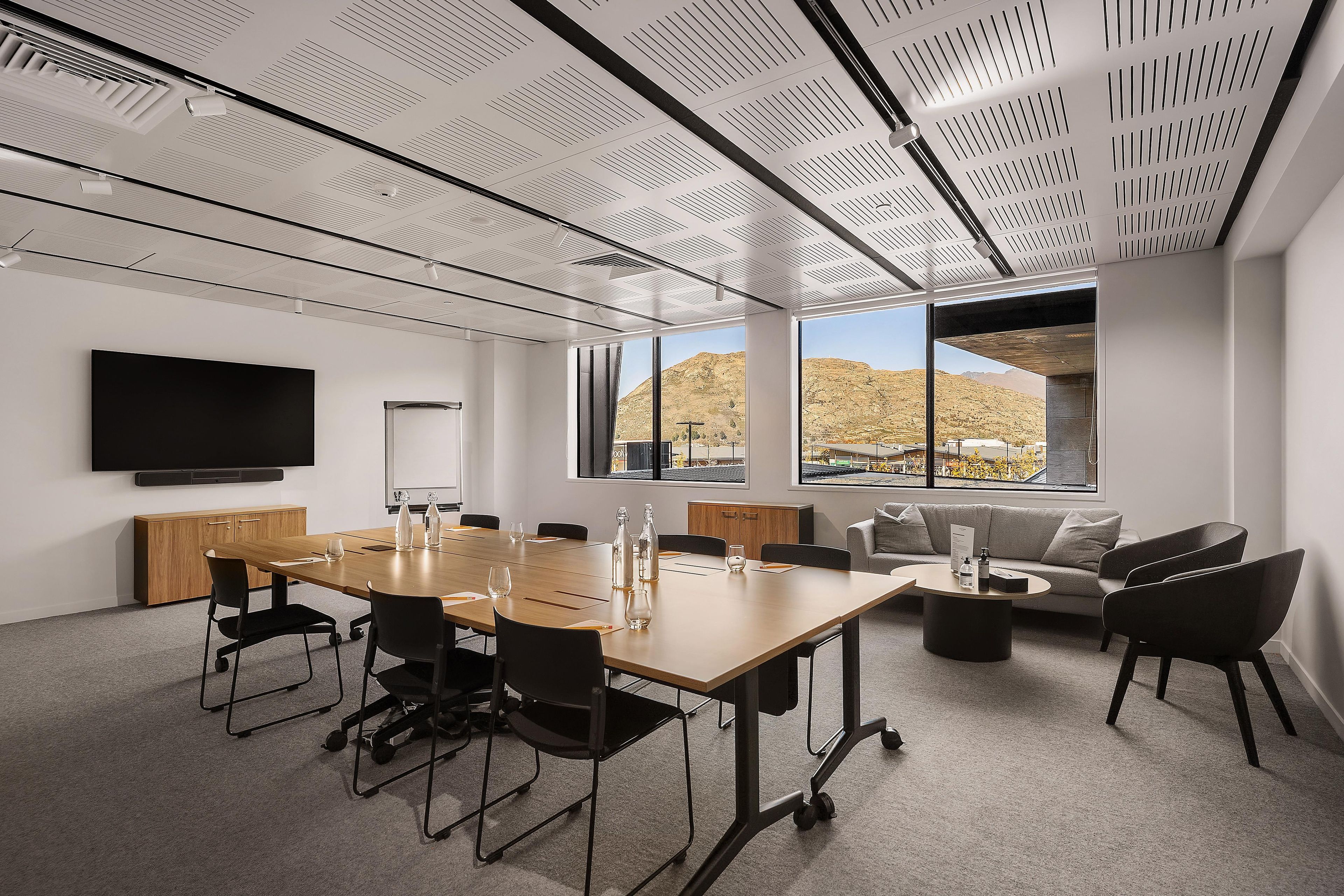 A conference room with a long table, chairs, a sofa, and a television on the wall.