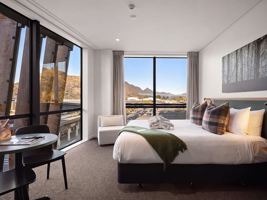 A hotel room with a large bed, a desk, and a view of mountains through the window.