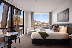 Habitación de hotel con una cama grande, un escritorio y vistas a las montañas a través de la ventana.