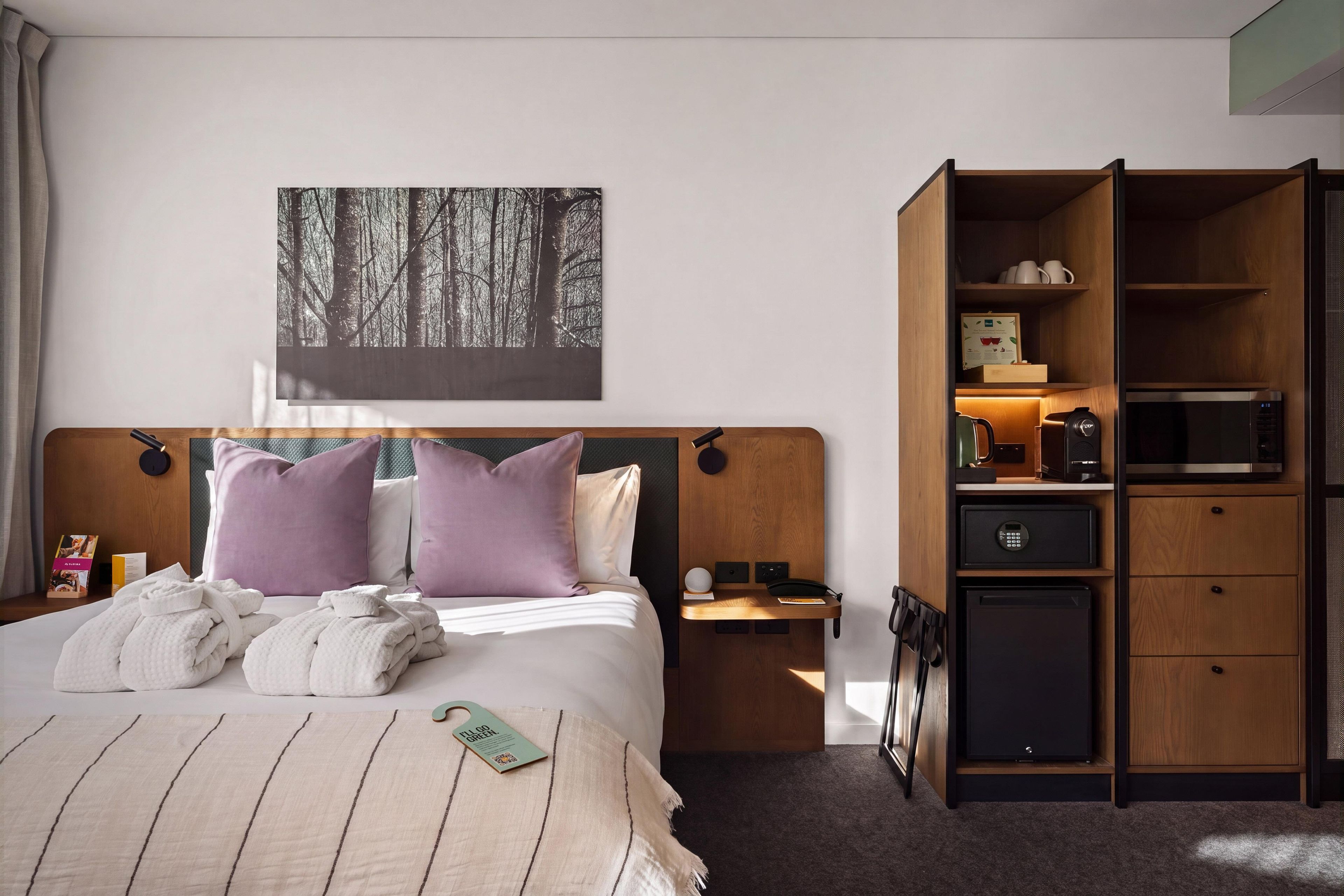 Une chambre d’hôtel avec un lit, une table de chevet, une armoire en bois et un tableau accroché au mur.