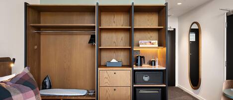 A hotel room with a bed, a desk, a wardrobe, a small kitchenette, and a mirror.