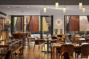A restaurant interior with multiple dining tables, chairs, pendant lighting, and large windows with decorative lattice.