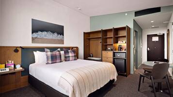 A hotel room with a bed, a desk, a chair, a wardrobe, and a painting on the wall.
