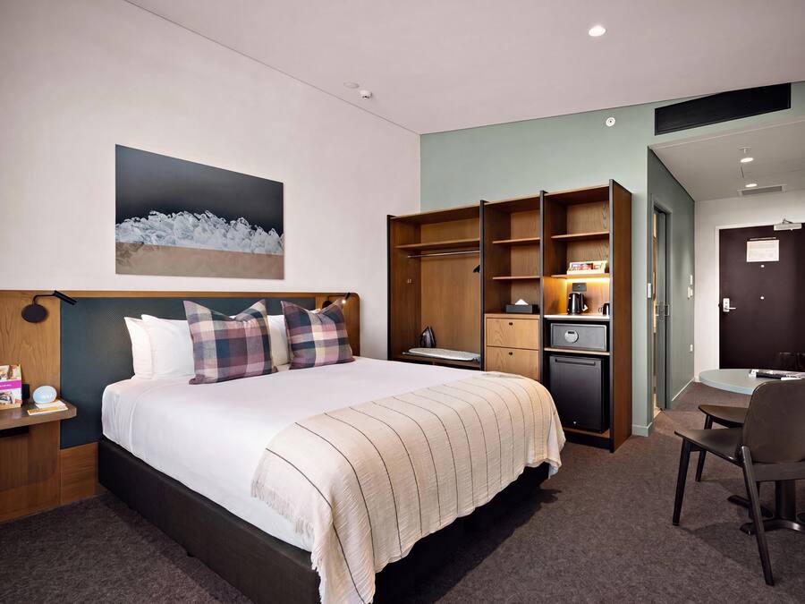 A hotel room with a bed, a desk, a chair, a wardrobe, and a painting on the wall.