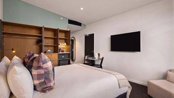A hotel room with a bed, a desk, a chair, a TV, and a wardrobe.