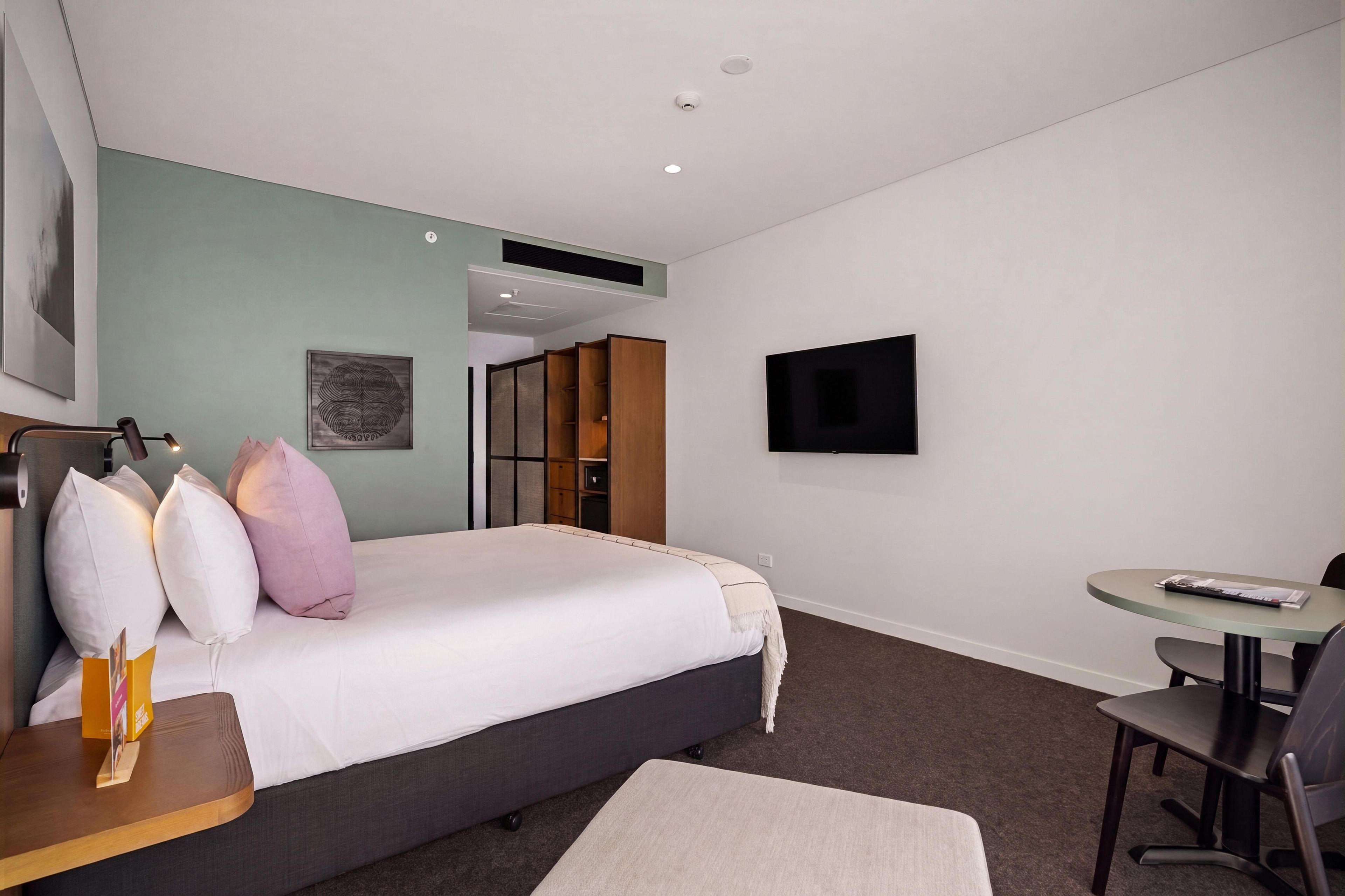 A modern hotel room with a bed, a desk, a chair, a television, and a large window.