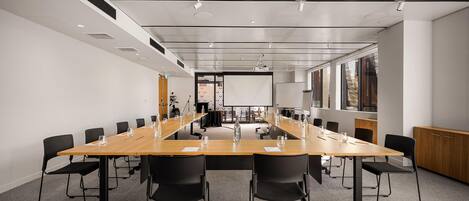 A conference room with a long table, black chairs, and a projector screen.