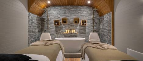 A modern bathroom with a freestanding bathtub, two beds with fur throw blankets, and wooden paneling on the ceiling.