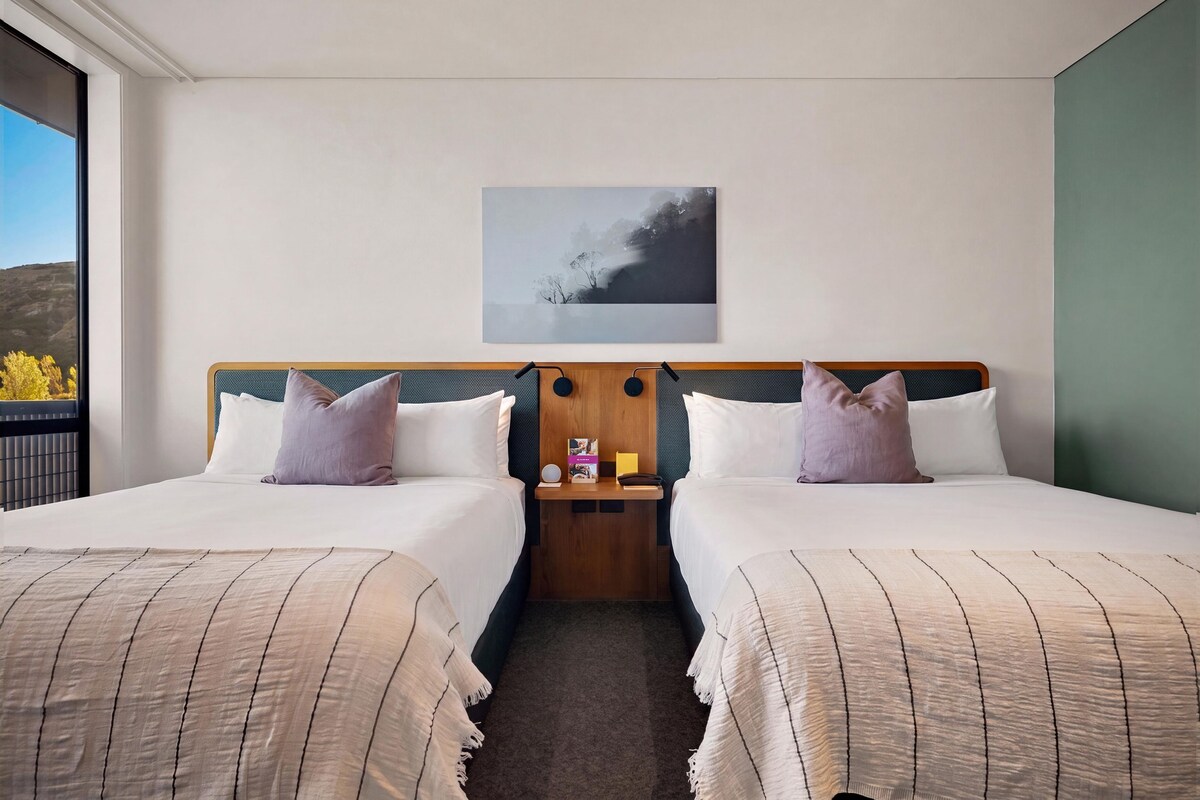 A hotel room with two beds, a nightstand, a lamp, and a painting on the wall.