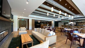 A spacious lobby with a sofa, chairs, a wooden table, a bar area, and a fireplace. - Sudima Queenstown Five Mile (Queenstown)