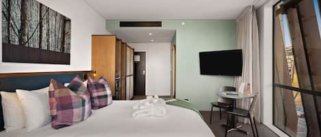 Habitación de hotel con una cama grande, escritorio, televisión y vistas al exterior.