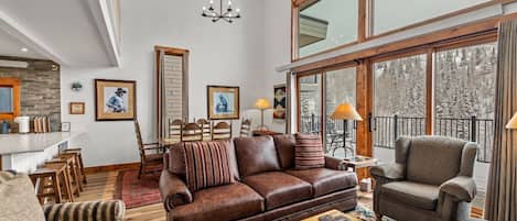A spacious living room with a brown leather sofa, a striped armchair, and a wooden coffee table.