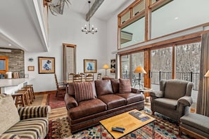 A spacious living room with a brown leather sofa, a striped armchair, and a wooden coffee table.