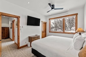 A bedroom with a bed, a ceiling fan, a TV, a window with a view of trees, and a wooden door. - Ski In/Out-Pool-HotTub-Views-Grill-Just Remodeled (Steamboat Springs)