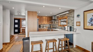 Eine moderne Küche mit Holzausstattung, einer großen Kochinsel mit Barhocker und einer Rückwand aus Stein.