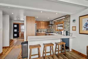 A modern kitchen with a central island, wooden bar stools, and a stone backsplash.