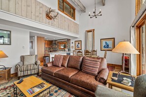 A spacious living room with a brown leather sofa, a wooden coffee table, and a high ceiling with exposed beams.