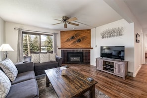 A living room with a sofa, coffee table, fireplace, television, and a ceiling fan.